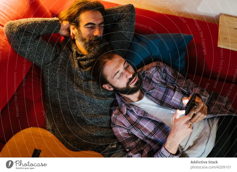 Hispanischer Vater und Sohn teilen sich ein Smartphone auf dem Sofa Zeit verbringen Wochenende Lächeln Porträt benutzend Apparatur Männer Gerät Zusammensein