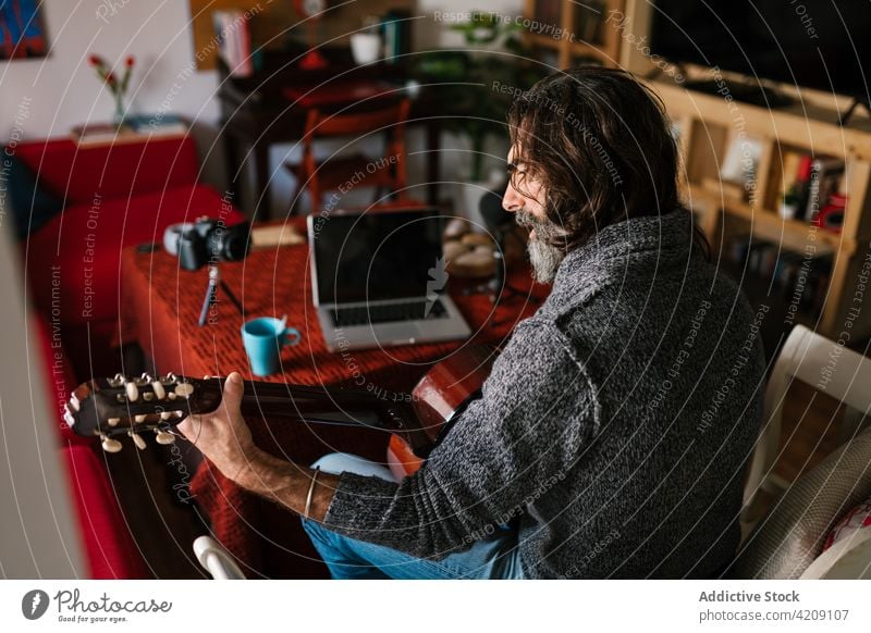 Hispanischer Gitarrist spielt Gitarre, während er ein Video auf dem Laptop betrachtet Gitarrenspieler spielen Lektion lernen Mann benutzend Apparatur Gerät