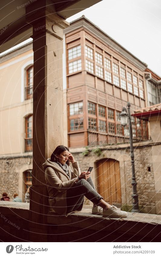 Frau, die mit ihrem Smartphone vor einem alten städtischen Gebäude chattet plaudernd Zeitvertreib Internet online Gesicht berühren ruhen urban benutzend
