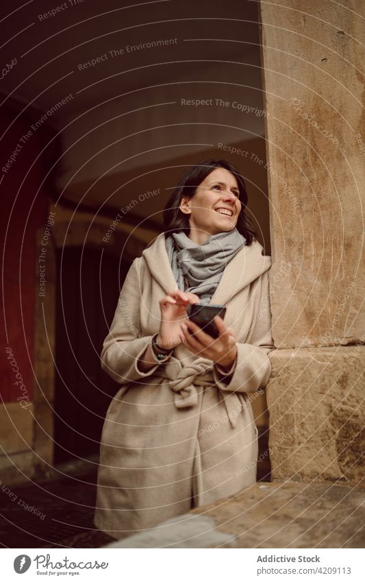 Frau, die mit ihrem Smartphone vor einem alten städtischen Gebäude chattet plaudernd Lächeln Zeitvertreib Internet online Gesicht berühren ruhen urban benutzend
