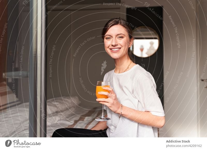 Glückliche junge Frau trinkt Saft auf dem Bett zu Hause trinken Inhalt Morgen Kälte frisch Gesundheit Getränk Komfort gemütlich Lächeln lässig Fenster Balkon