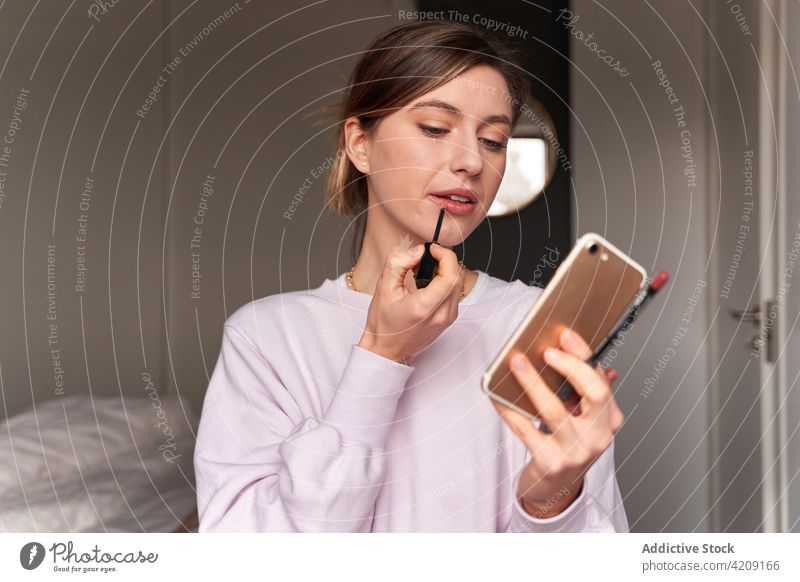 Junge Frau malt ihre Lippen während eines Video-Chats Malerei vlog Smartphone manifestieren Lipgloss Internet Blogger online Mobile Telefon jung lässig Glück
