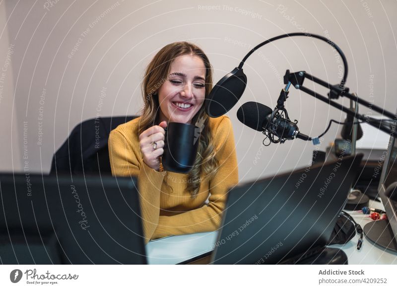 Fröhliche Frau mit Kaffee im Gespräch mit dem Mikrofon in einem Rundfunkstudio Arbeit Radio Ausstrahlung Atelier Aufzeichnen Laptop reden Tasse Becher