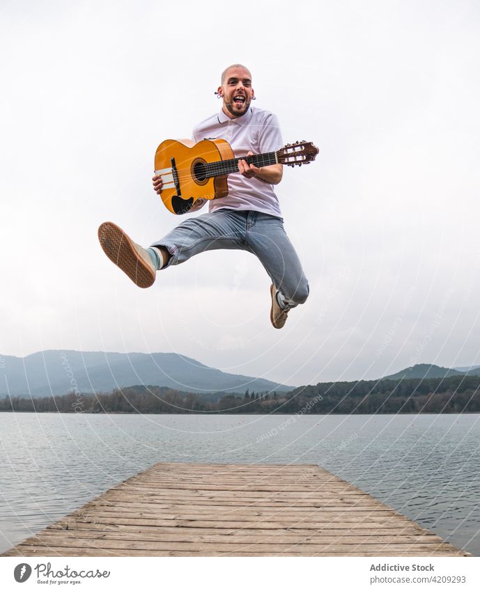 Mann springt mit Gitarre auf dem Steg gegen den Fluss springen Pier Freiheit Inspiration Künstler See Musiker Berge u. Gebirge Gitarrenspieler Natur Ufer