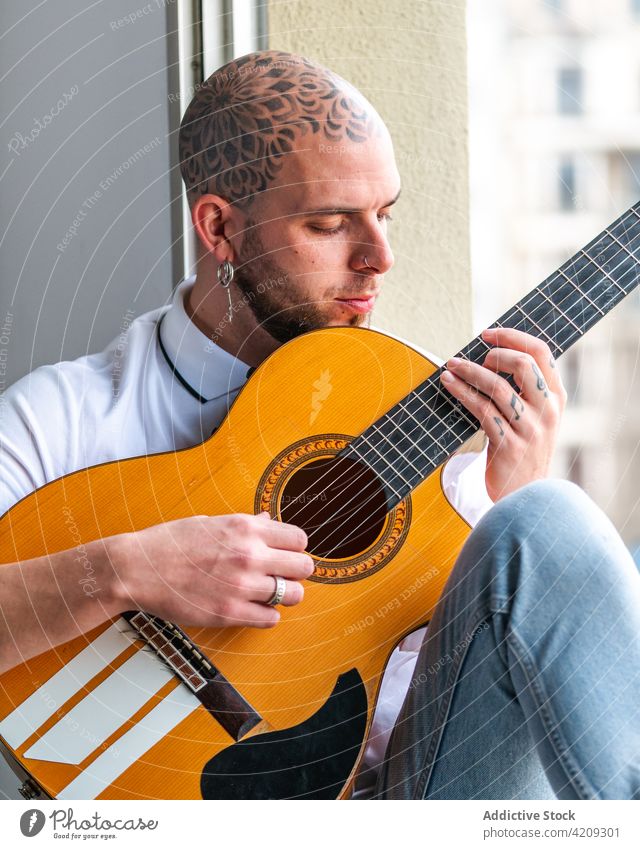 Musiker sitzt am Fenster und spielt tagsüber Gitarre Mann Tattoo spielen Melodie Hobby Mandala besinnlich ausführen männlich Gitarrenspieler Fokus kahl