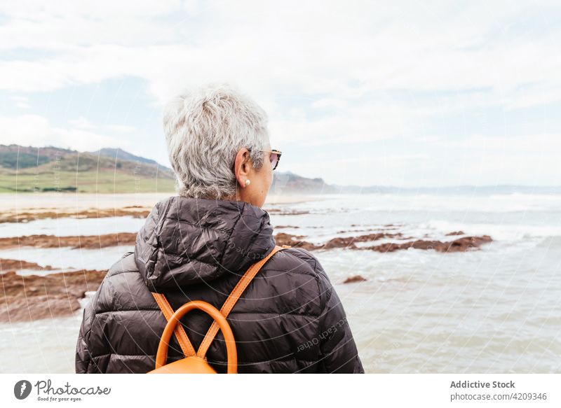 Anonymer älterer Wanderer bewundert das Meer unter bewölktem Himmel bewundern Wanderung genießen Natur Meereslandschaft Frau nachdenken Mast Trekker MEER