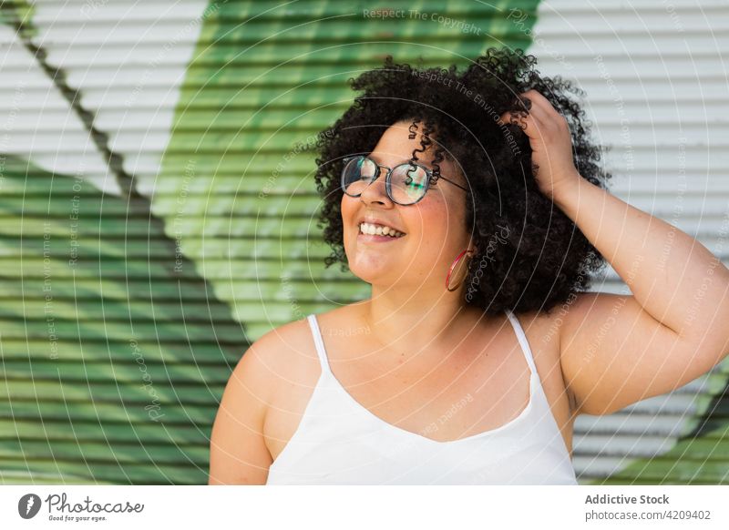 Glückliche mollige Frau mit Brille vor gerippter Wand Haare berühren Lachen herzlich freundlich Afro-Look charmant Porträt Übergewicht genießen Lächeln Ornament