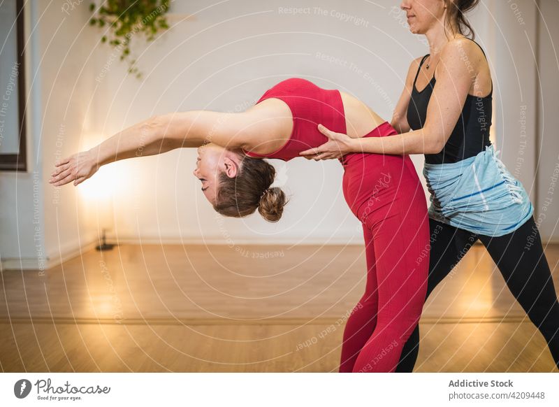 Flexible Frau, die ihren Körper mit einem Ausbilder dehnt Frauen Ausbilderin zurückbiegen Yoga Hilfsbereitschaft Dehnung beweglich Asana Zusammensein üben