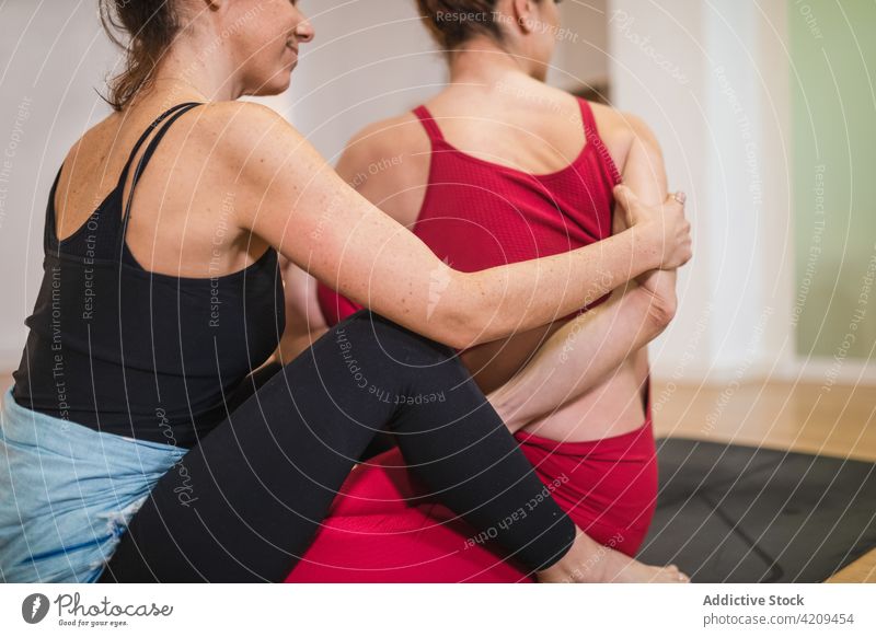 Trainerin hilft Frau bei Dehnungsübungen Frauen Asana Yoga verdrehen Hilfsbereitschaft Wohlbefinden Klasse positionieren üben Zusammensein Ausbilderin abstützen