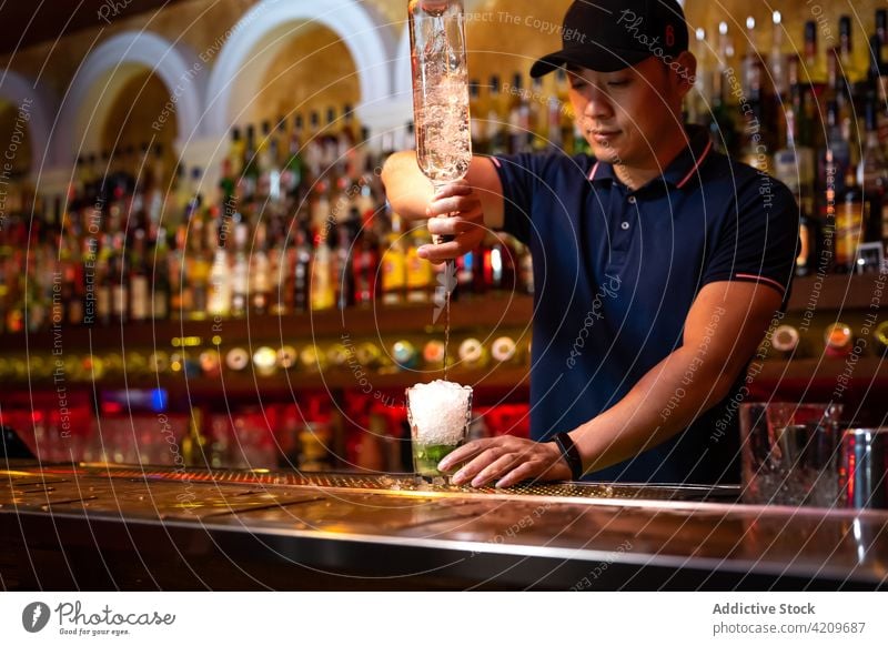 Junger asiatischer Barkeeper gießt Rum in ein Glas, während er einen Cocktail in der Bar zubereitet Alkohol alkoholisch Aperitif Barista Barmann Getränk Flasche