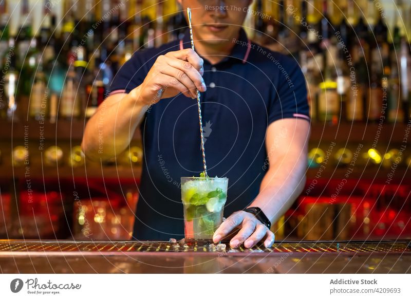 Unbekannter Barkeeper, der das Glas hält und den Mojito-Cocktail in der Bar umrührt Alkohol alkoholisch Aperitif Barista Barmann Getränk Flasche Business Club