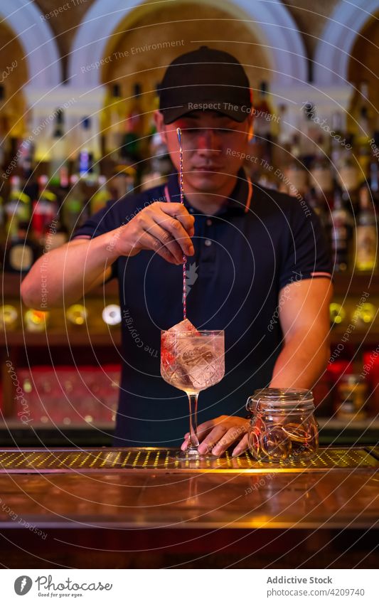 Junger asiatischer Barkeeper rührt einen Gin-Tonic-Cocktail mit einem Löffel in der Bar Alkohol alkoholisch Aperitif Barista Barmann Getränk Flasche Business