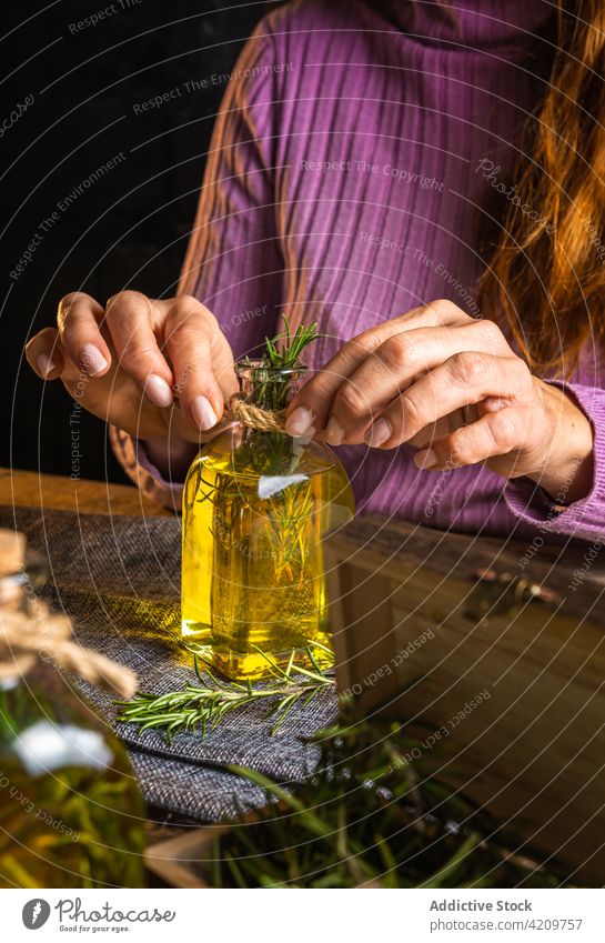 Unbekannte Frau demonstriert Flasche mit Öl und Rosmarin Kraut Erdöl manifestieren Stoff Tisch Glas zeigen filigran notwendig Licht purpur lässig kreativ
