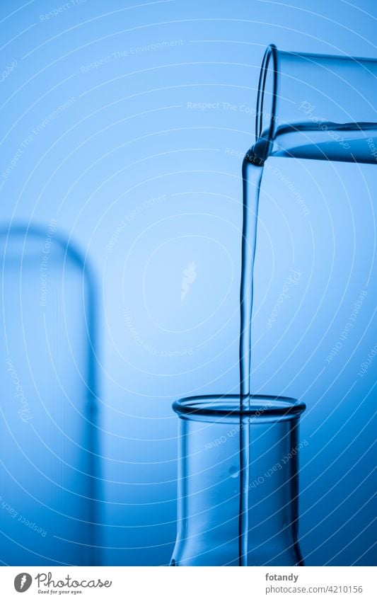 Befüllen eines Erlmeyer-Kolbens aus einem Reagenzglas vor blau getöntem Studio-Hintergrund. analysieren befüllen Bewegung Chemie Chemielabor Design drogen