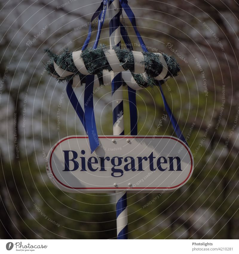 Schild "Biergarten" ist an einem Maibaum mit Kranz und blauen Bändern befestigt. grün weiß Menschenleer Farbfoto Außenaufnahme Tag Tradition Frühling