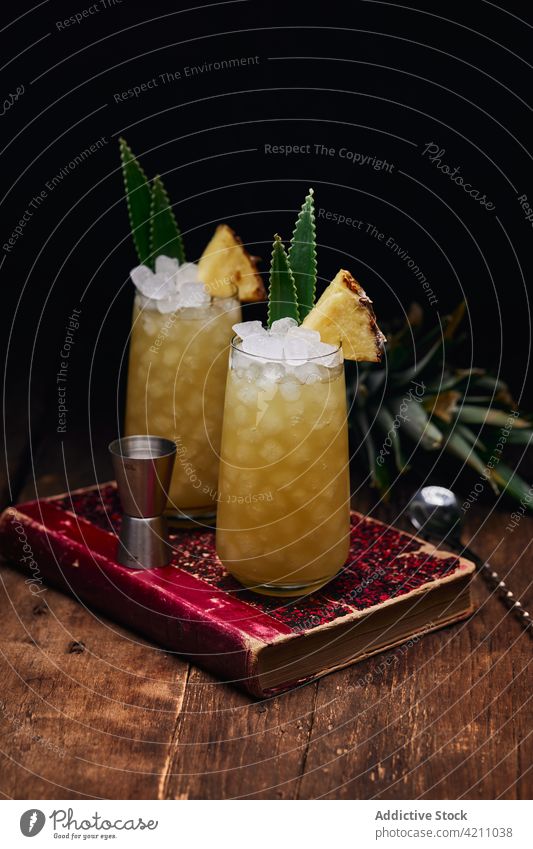 Gläser mit Cocktails mit Ananasstücken auf Buch Glas Eis Erfrischung Tisch Blatt trinken Löffel Getränk Frucht Alkohol geschmackvoll kalt lecker Portion