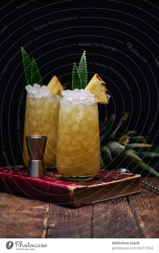 Gläser mit Cocktails mit Ananasstücken auf Buch Glas Eis Erfrischung Tisch Blatt trinken Löffel Getränk Frucht Alkohol geschmackvoll kalt lecker Portion