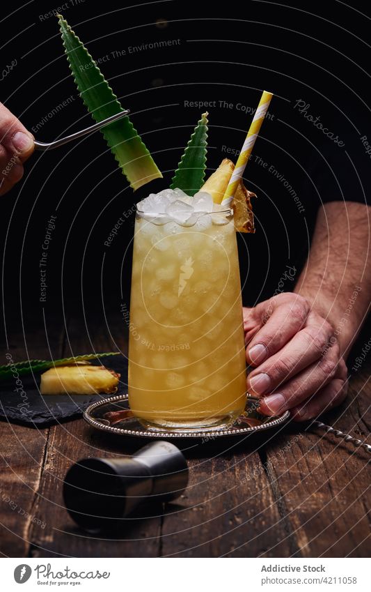 Gesichtsloser Barkeeper dekoriert Cocktailglas mit Ananasblättern Garnierung Glas Würfel Stroh Tablett Tisch männlich Blatt Restaurant Mann
