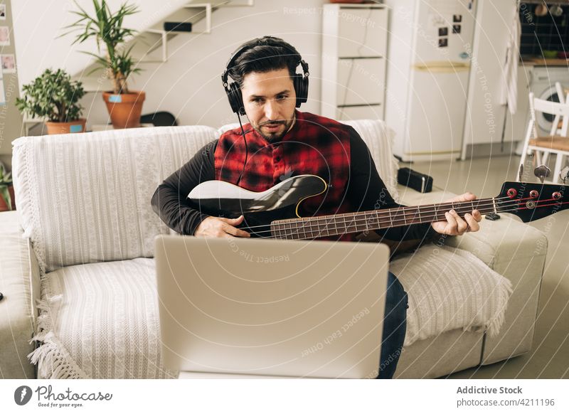 Bassist mit Headset spielt Gitarre gegen Laptop zu Hause spielen Lektion lernen Bildung Mann benutzend Apparatur Gerät Kopfhörer Gitarrenspieler Video heimwärts