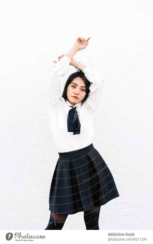 Selbstbewusste asiatische Frau mit über dem Kopf gekreuzten Händen Schüler Uniform cool selbstbewusst starren Individualität Körperhaltung elegant Starrer Blick