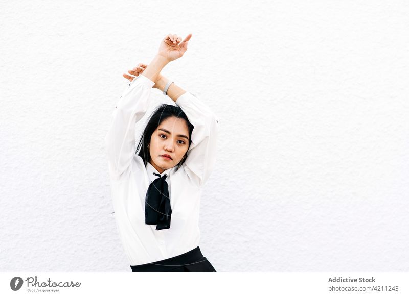 Selbstbewusste asiatische Frau mit über dem Kopf gekreuzten Händen Schüler Uniform cool selbstbewusst starren Individualität Körperhaltung elegant Starrer Blick