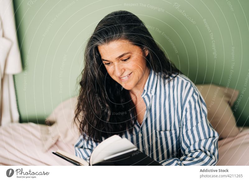 Nachdenkliche ethnische Frau sitzt im Bett und liest einen Roman lesen Buch besinnlich sich[Akk] entspannen sitzen Hobby ruhig Literatur friedlich interessant