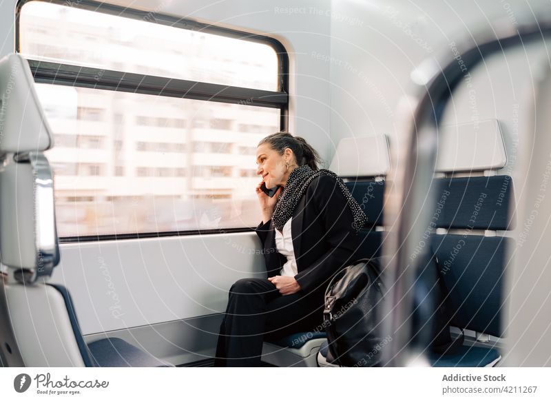 Fröhliche Frau spricht im Zug am Telefon Passagier Sitz Fenster Telefonanruf Gespräch Smartphone reden Arbeitsweg Ausflug Abenteuer Reise Schal Tasche
