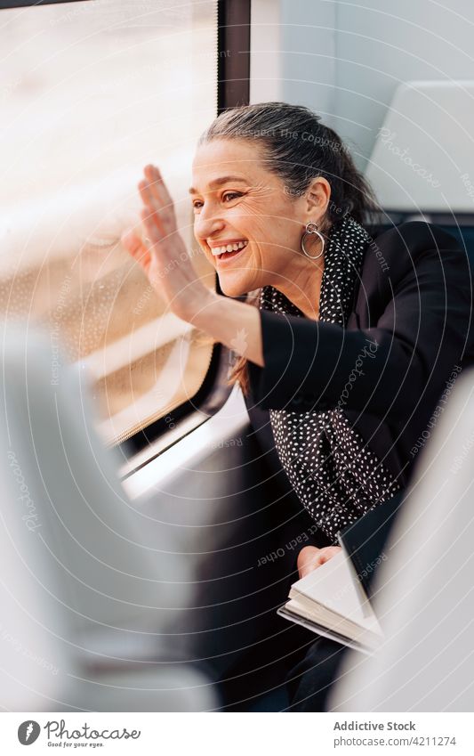 Lächelnde Frau mit winkender Hand im Zugfenster Wellenhand Gruß Fenster Ausflug Reise Passagier Wagen Arbeitsweg Abenteuer reif Lebensmitte reflektieren Schal