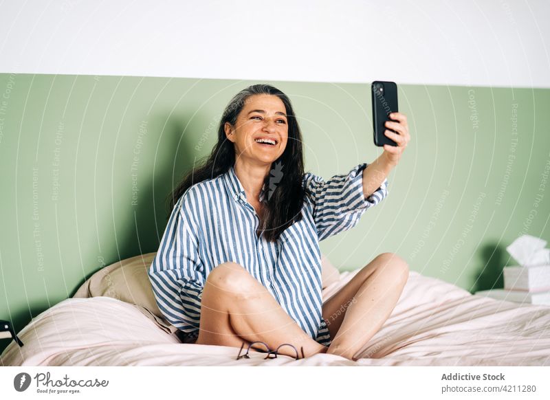 Zufriedene reife hispanische Frau, die ein Selfie auf dem Bett macht Lächeln Smartphone selbstbewusst heiter sich[Akk] entspannen Schlafzimmer soziale Netzwerke