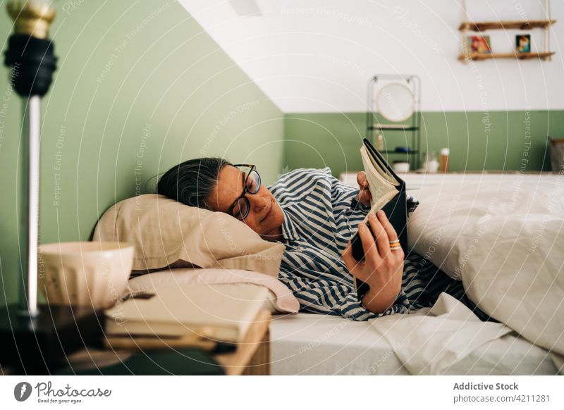 Nachdenkliche ethnische Frau liegt im Bett und liest einen Roman lesen Buch Lügen besinnlich sich[Akk] entspannen Hobby ruhig Literatur friedlich interessant