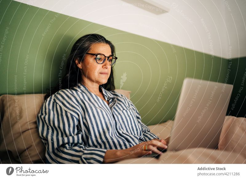Selbstbewusste reife hispanische Dame, die im Bett aus der Ferne an einem Netbook arbeitet Frau Arbeit Laptop freiberuflich abgelegen online Internet Anschluss