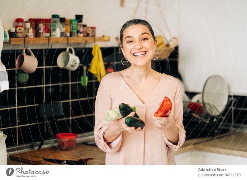 Glückliche reife Frau mit Gemüse in der Küche Paprika Salatgurke Porree Geschirr Lebensmittel Bestandteil Abfertigungsschalter gesunde Ernährung Lächeln heiter