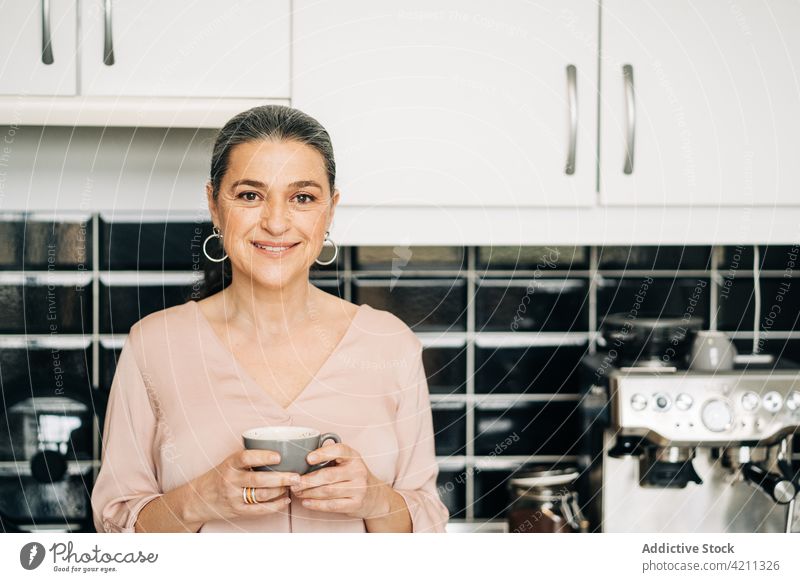 Glückliche reife Frau mit einer Tasse Kaffee in der Küche Kaffeemaschine Gerät trinken heimisch Küchengeräte Schrank Lebensmitte Lächeln heimwärts genießen