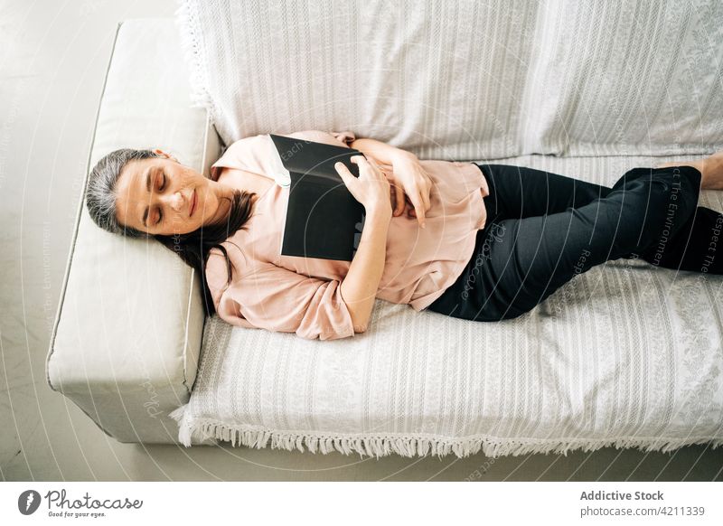 Reife Frau mit Buch schlafend auf Couch Liege Sofa ruhen Appartement heimisch Mittagsschlaf Hobby Leseratte Wohnzimmer heimwärts lässig Komfort flach