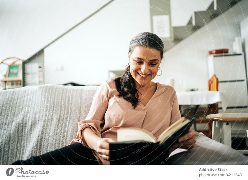 Konzentrierte Frau, die auf der Couch ein Buch liest lesen Lächeln Liege Sofa Appartement Glück heimisch Hobby Leseratte froh Wohnzimmer heimwärts lässig
