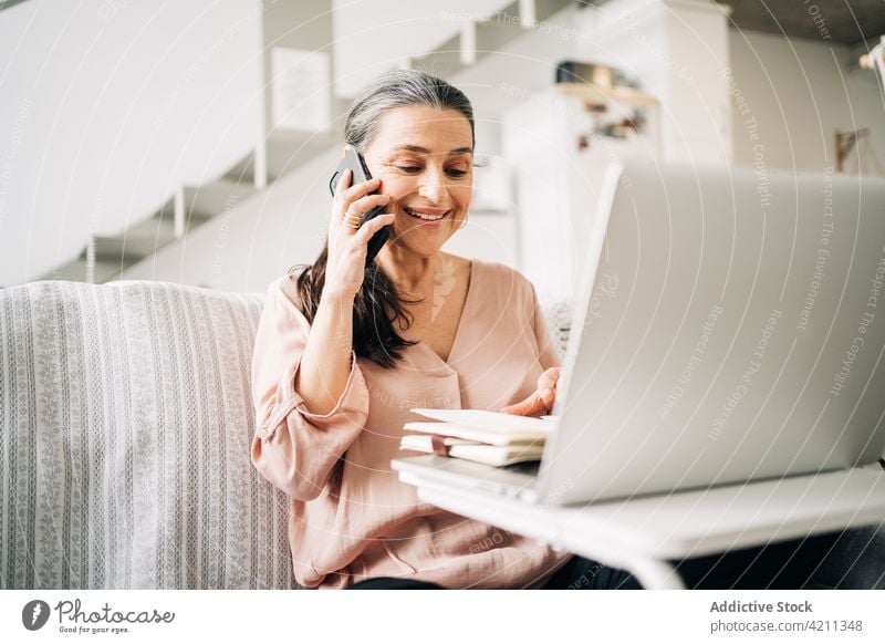 Seriöse reife Frau, die mit einem Smartphone spricht und in ein Notizbuch schreibt Telefonanruf reden schreiben Notebook Kommunizieren Laptop