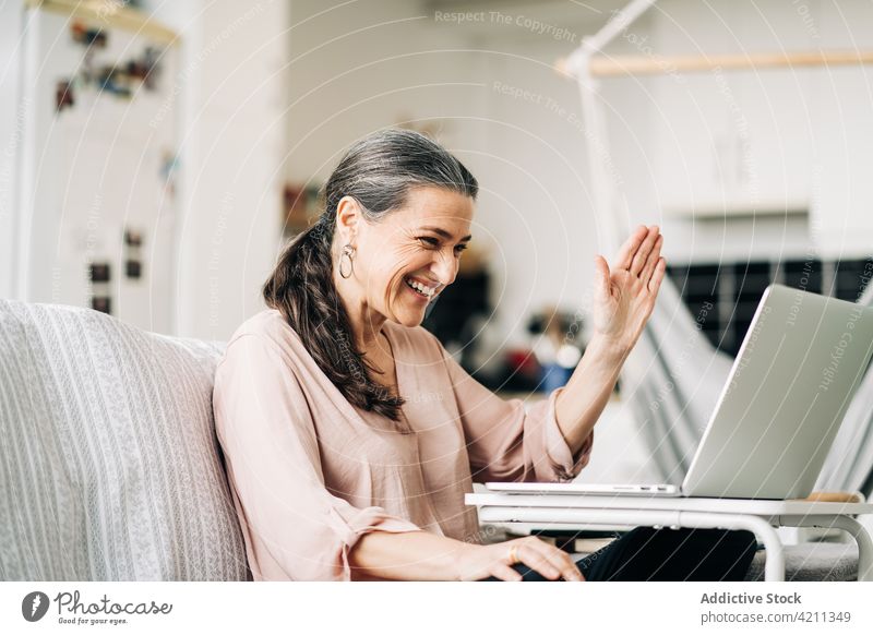 Fröhliche reife Frau, die ein Videogespräch über einen Laptop führt Videoanruf Video-Chat winkend Liege Kommunizieren Internet Gespräch Raum online flach Hi