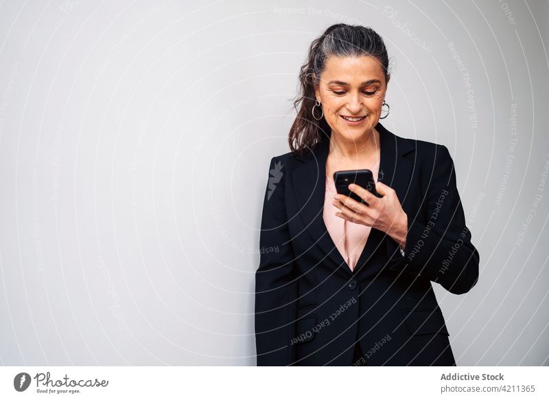 Selbstbewusste reife Frau im Anzug beim Surfen auf dem Smartphone Lächeln Browsen Textnachricht Unternehmer Glück formal Manager respektabel froh Business SMS