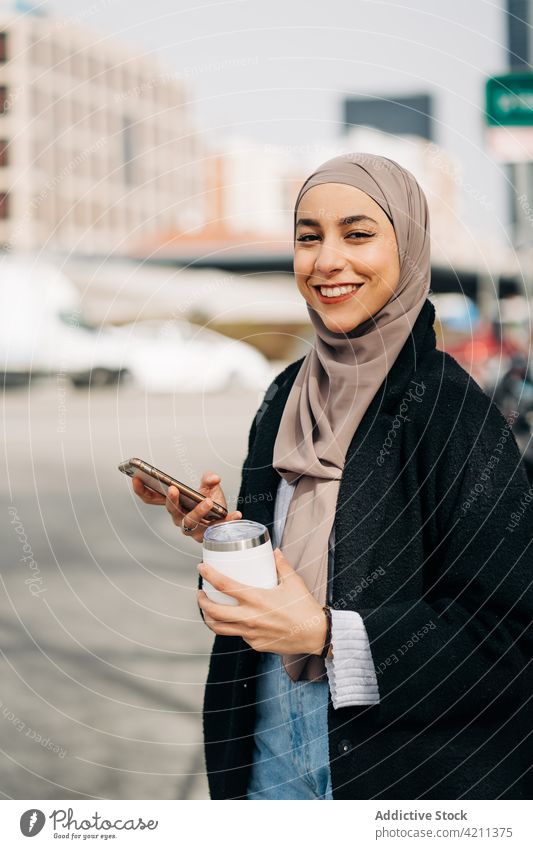 Fröhliche stilvolle muslimische Frau beim Surfen auf dem Smartphone in der Stadt Nachricht Großstadt Imbissbude trinken genießen Spaziergang Hijab ethnisch