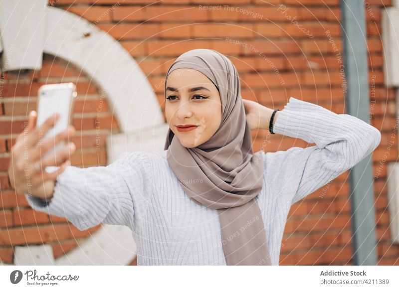 Charmante ethnische Frau mit Kopftuch macht ein Selfie in der Stadt Großstadt Smartphone Selbstportrait Hijab heiter unterhalten charmant muslimisch Tradition