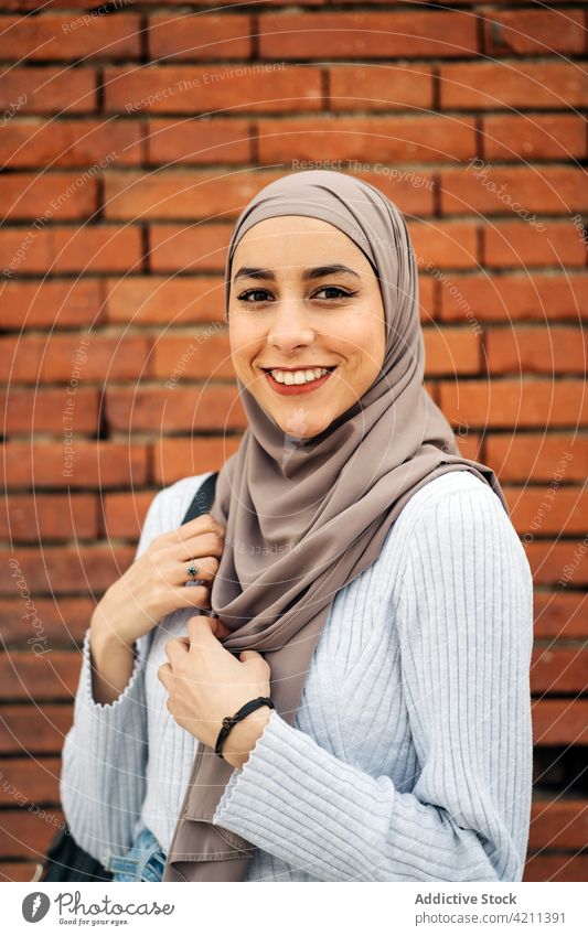 Gelassene ethnische Frau im Hidschab schaut in die Kamera in der Stadt Kopftuch Hijab Tradition Großstadt charmant Outfit Straße Stil Kultur muslimisch Baustein