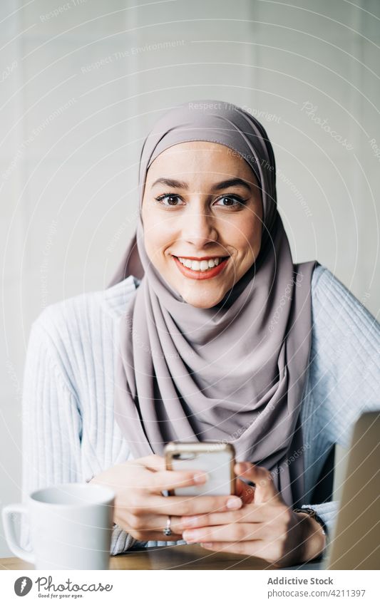 Porträt einer muslimischen Unternehmerin mit Smartphone Frau Arbeit freiberuflich Café benutzend ethnisch Tisch abgelegen Apparatur Gerät Funktelefon Mobile