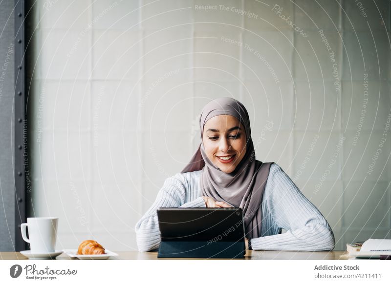 Entzückte ethnische Frau mit Videoanruf auf dem Tablet Video-Chat Gruß Hallo Tablette reden Hi Hijab muslimisch Tisch Café Inhalt heiter Kommunizieren Apparatur
