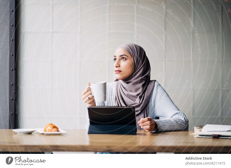 Nachdenkliche muslimische Frau mit Getränk und Tablet in einem Cafe Café freiberuflich Arbeit nachdenklich Tablette Tasse trinken besinnlich Hijab ethnisch