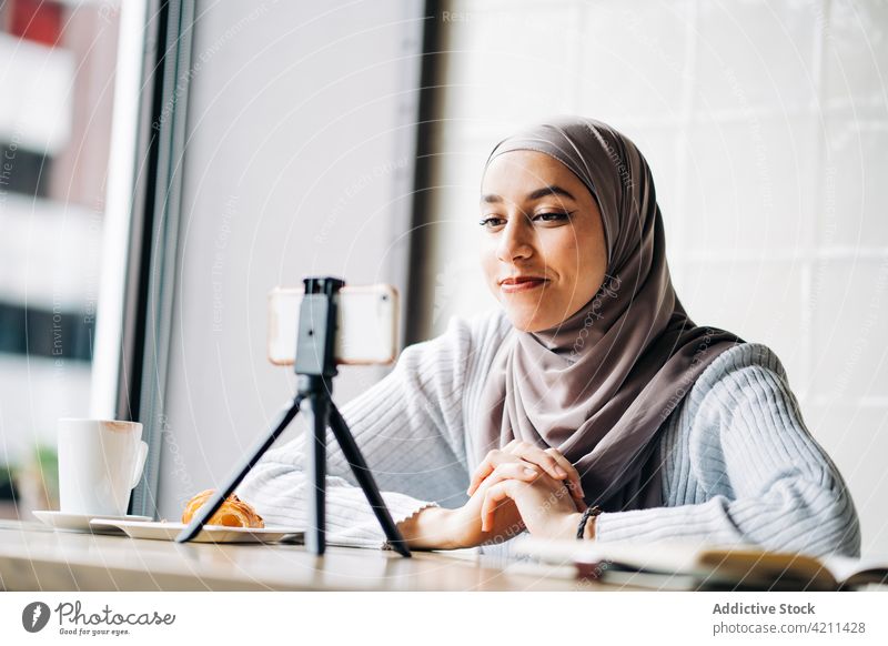 Lächelnde ethnische Frau, die in einem Café ein Video für einen Blog aufnimmt Blogger Aufzeichnen Smartphone Influencer soziale Netzwerke benutzend muslimisch