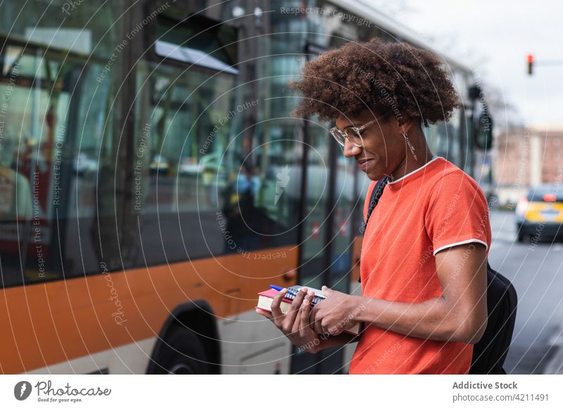 Lächelnder junger Afroamerikaner, der vor dem Studium am Straßenrand steht Mann Großstadt Inhalt trendy Bus Persönlichkeit cool selbstbewusst urban männlich
