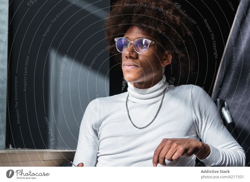 Stilvoller junger afroamerikanischer Mann chillt im Café im Sonnenlicht Kälte besinnlich Mode allein Erholung Vorschein Persönlichkeit ruhig Individualität