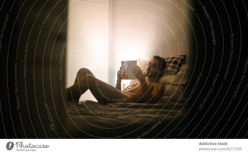 Nackter Mann liegt auf dem Bett und liest ein Buch lesen nackt Schlafzimmer sich[Akk] entspannen gemütlich Abend männlich itim interessant Roman Belletristik