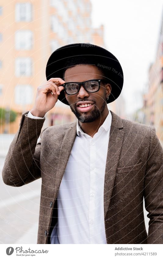 Trendiger schwarzer Mann steht auf der Straße und schaut in die Kamera Stil Hut Jacke gutaussehend Brille trendy maskulin Großstadt männlich ethnisch