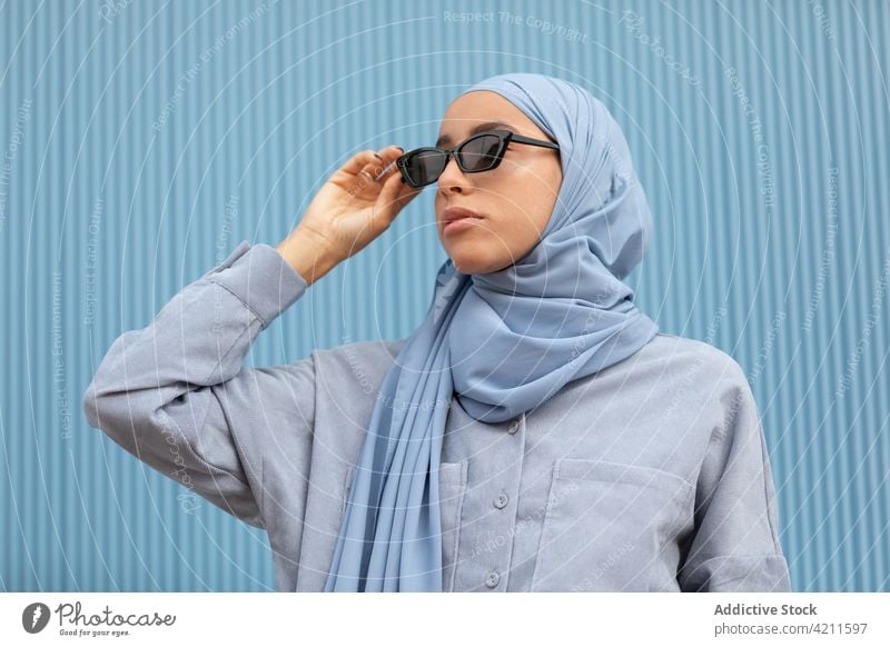 Trendige muslimische Frau mit Sonnenbrille auf blauem Hintergrund Mode Stil Kopftuch nachdenken Individualität Accessoire Islam Porträt lässig cool modern Farbe